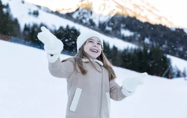 Criança sorri enquanto brinca com flocos de neve