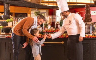 chefe dando comida para criança enquanto seu pai sorri