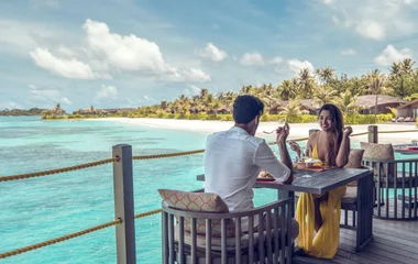 Casal almoçando em cenário paradisíaco.