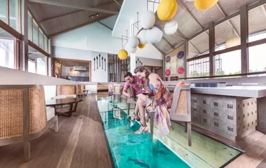 Casal observando os peixes na água através do vidro do chão do resort.