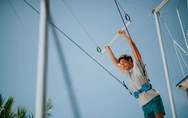 Um homem de camisa cinza e short azul se preparando para saltar do trapézio voador