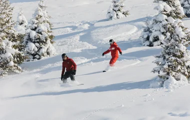 Dois homens fazem manobras de snowboard na neve.