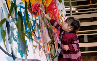 Criança desenhando com tinta numa tela branca com pinceladas coloridas.