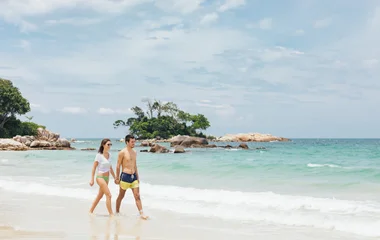 Casal de maõs dadas andando pela água em praia paradisíaca