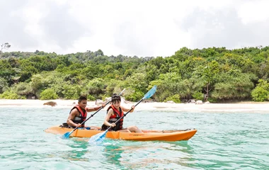 Pessoas praticando caiaque em um mar com um cenário de mata atrás.