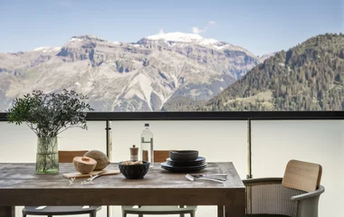 Varanda de chalé alpino de luxo com vista panorâmica das montanhas, mesa posta e cadeira no centro da varanda,