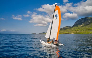 Um barco a vela no meio da água em um cenário de montanhas verdes.