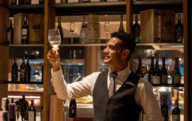Sommelier Club Med balançando uma taça de vinho em uma adega.
