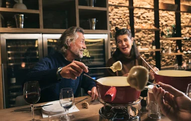 Homem e mulher de 40 anos comendo fondue em mesa posta num restaurante