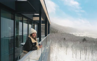 Mulher na varanda do quarto apreciando a paisagem na neve.
