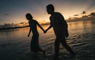 Casal caminhando em praia paradisíaca ao pôr do sol em destino tropical