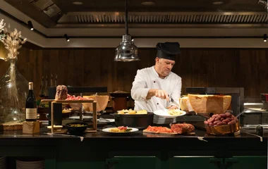 Um chefe preparando um prato em meio a uma mesa farta.