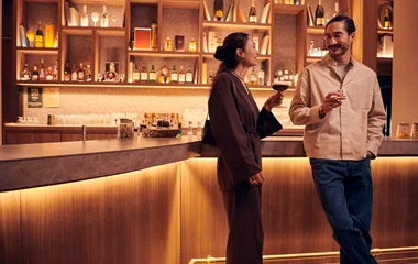 Casal bebe vinho em pé encostados no bar premium do Club Med