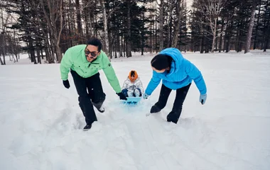 Padre, madre e hija jugando en la nieve.