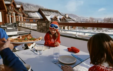 Familia a punto de recibir una pizza en su mesa en un restaurante con vista a las montañas.