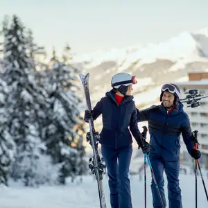 Casal se olhando enquanto caminham na neve com os equipamentos de esqui.