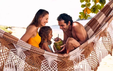 Mãe, pai e filha numa rede na praia.