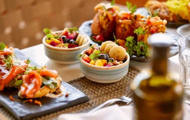 Dos cuencos de ensalada de frutas al lado de un plato con acarajé y otro con entradas de salmón fresco.