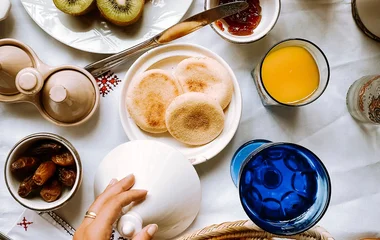 Mesa de café da manhã servida com frutas, pães, sucos e geleia.