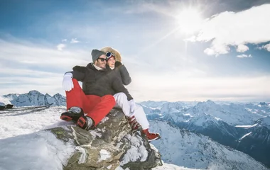 Casal sentado uma paisagem de neve num dia de sol.