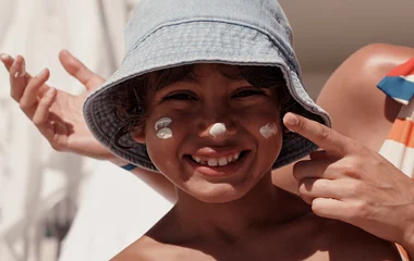Menino sorridente com protetor solar nas bochechas.
