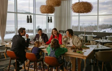 Família sentada à mesa do restaurante no almoço com as montanhas de neve ao fundo das grandes janelas