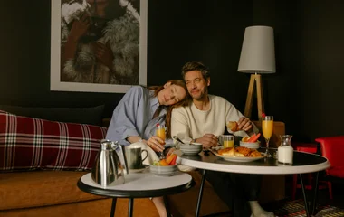 Mulher com o rosto encostado no ombro do companheiro enquanto tomam café da manhã.