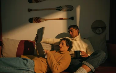 Casal sentado em um sofá, lendo um jornal e tomando café