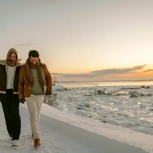 Casal andando de mãos dadas em montanha nevada ao por do sol