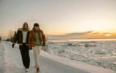 Casal andando de mãos dadas em montanha nevada ao por do sol