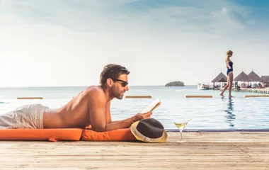 Homem deitado ao lado de um chapéu enquanto lê.