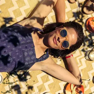 Mujer tumbada boca abajo con gafas de sol y los brazos bajo la cabeza con un top estampado azul