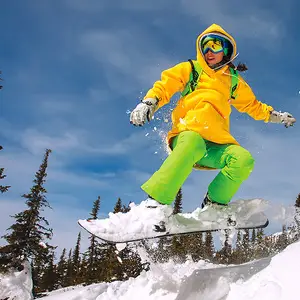 Pessoa com roupa amarela e verde saltando com a prancha de snowboard.