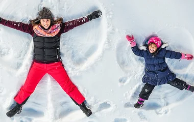 mãe e filha fazendo bonecos de neve usando roupas de esportes representando o que é um casaco para neve