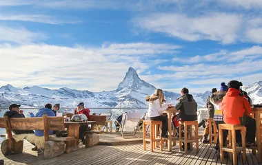 Pessoas sentadas, comendo e bebendo na estação de Zermatt.