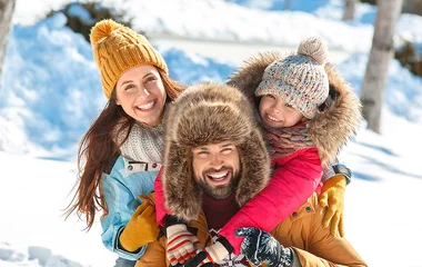 Pai, mãe e filha sorrindo na neve.