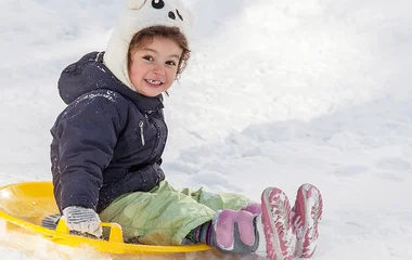 Criança se divertindo na neve com disco de plástico.