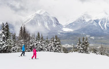 vista panoramica de pista de esqui com duas pessoas praticando em frente a montanha