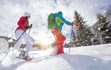 Casal caminhando na neve de raquete.