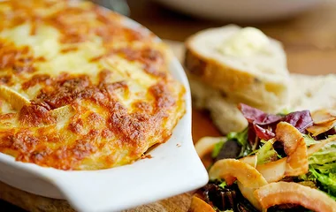 Tartiflette em uma travessa branca de cerâmica ao lado de uma salada.