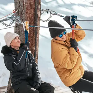 Duas pessoas descendo de tirolesa numa paisagem de neve.