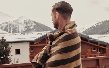 Homem com toalha enrolada no corpo, observando as montanhas cobertas de neve ao fundo