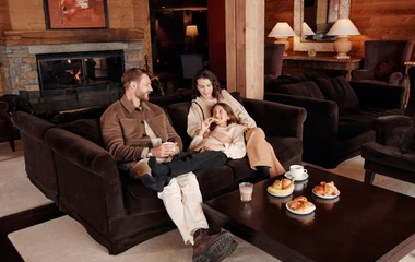 Família em resort de neve do Club Med, sentados no sofá, conversando.