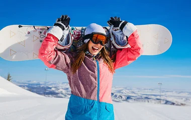 Mulher usando roupa de snowboard e segurando a prancha com as duas mãos.