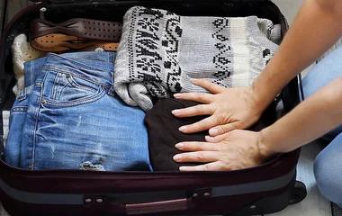 Mulher apertando as roupas da mala de viagem para colocar outras.