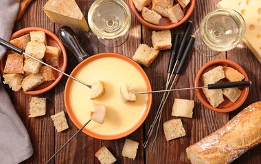 Mesa com fondue de queijo e acompanhamentos.