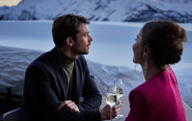 Casal com duas taças de espumante em paisagem dos Alpes.