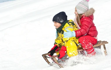 Duas crianças descendo na neve num trenó de madeira.