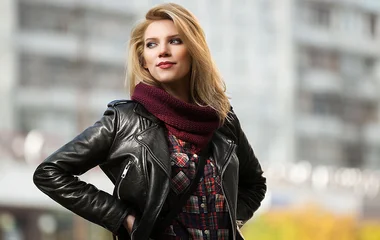 Mulher de jaqueta de couro e encharpe olhando para o lado.