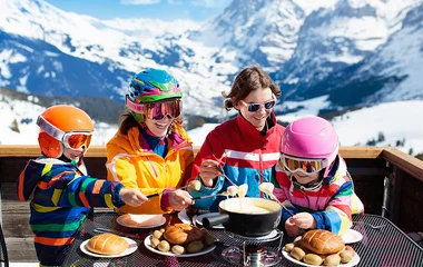 Família comendo fondue ao ar livre com as montanhas de fundo.